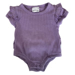 A baby's short-sleeve waffle-knit bodysuit in lavender purple, laid flat on a speckled stone countertop. The bodysuit features ruffled cap sleeves and a ribbed neckline.